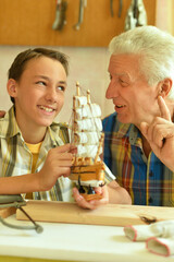Cute boy with grandfather making wooden model