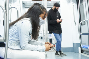 An African American girl and a Caucasian boy using the smartphone in the subway car. Young people in public transport abducted by technology.