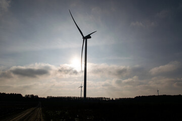 Obraz premium Sunlight view of a giant wind turbine standing in the middle of a field against a blue sky with white clouds