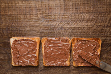 Toast with chocolate-nut paste spread on wooden background top view with copy space.