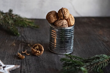 Walnuts in a tin Cup with spruce twigs and a wooden star on a wooden table. Christmas card. Low key