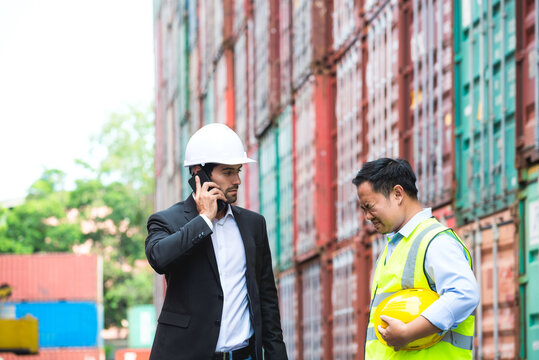Labor or worker is apologizing to business man or boss about his mistake and boss is reporting to high level about problem impact with cargo container stacked in background. Concept of mistake working