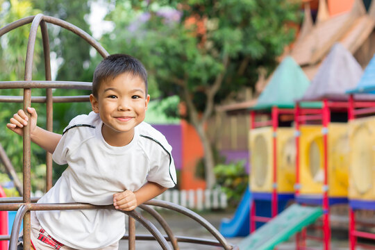 Portrait image of 6-7 years old boy. Happy Asian child boy play the toy and climbing the steel toy bar at the playground. He smiling. Sport and exercise of kid.