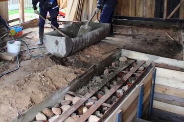 Two workers mix cement mortar with a water in a large basin against the background of reinforced...
