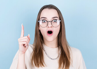 Close-up portrait of charming young woman in eyeglasses pointing with finger, looking at camera, isolated on blue background