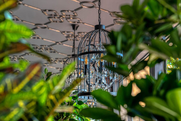 A large pendant lamp hangs in a restaurant between green plants.