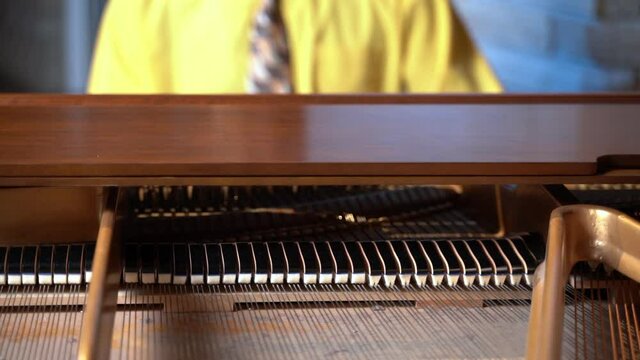 Man in yellow shirt playing open piano dusty interior hammers moving