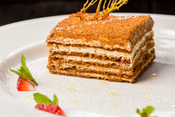 fresh delicious honey cake on white plate on black background