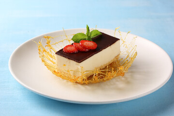 Dessert. Bird milk cake with strawberries and mint. Sponge cake, souffle and chocolate ganache, caramel on a white plate on a blue table. Background image, copy space, horizontal