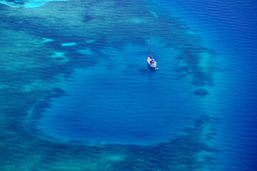 Fototapeta na wymiar White yacht floating above a coral reef in beautiful bay. Aerial view
