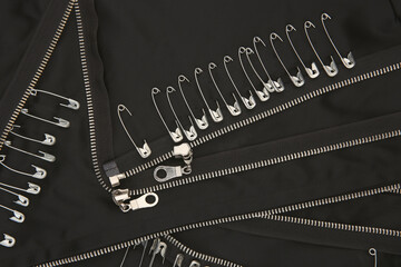 Safety pins and zippers on black fabric. Close up of subculture clothing.