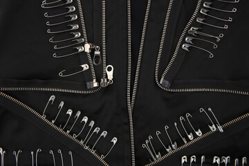 Safety pins and zippers on black fabric. Close up of subculture clothing.