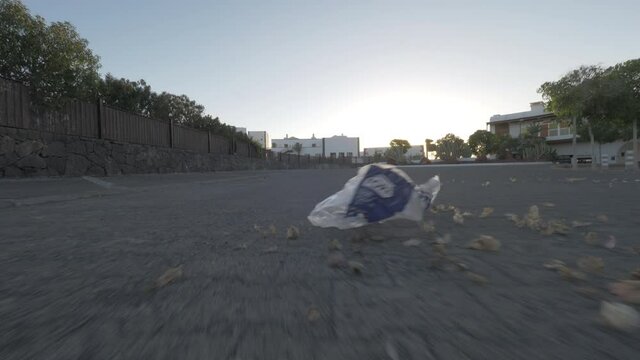 Point of view shot of wind blowing dry leaves and plastic bag along empty city street. Urban litter