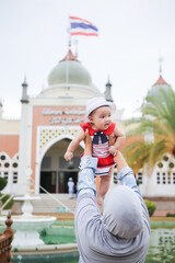 An Asian Muslim mother is holding her baby in front of a mosque.