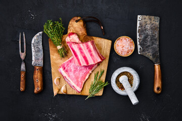 Raw lamb breast ribs on wooden cutting board with herbs and seasoning