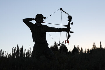 silhouette of American bow hunter drawing bow back in woods