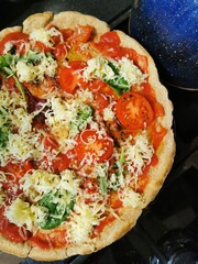  round pizza with red tomatoes, cheese, herbs on a dark background