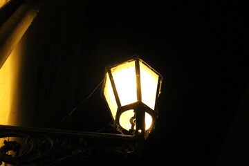 an old street lamp, lit at night, with a spider web attached