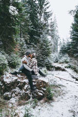 Happy couple kissing on rock in snowy forest