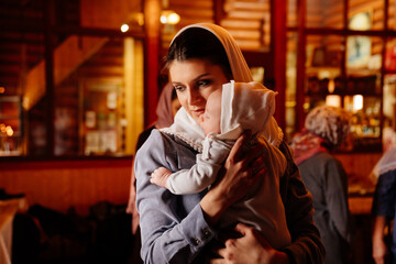 beautiful mom in a headscarf with a small child in her arms in church. 