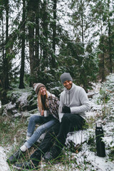 Happy couple with mugs of hot drink in snowy forest
