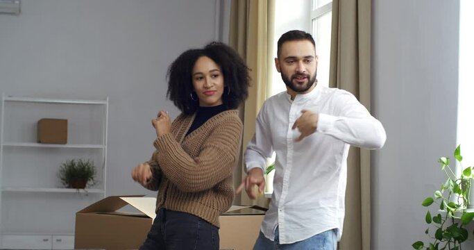 Moving footage cropped view young people black woman african american girlfriend wife and caucasian man husband in white shirt dancing funny dancing next to boxes celebrating real estate purchase home