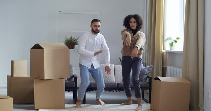 Full height filming funny comic young couple friends wife and husband boyfriend and girlfriend dancing move together posing for camera rejoice at buying new home filming real estate, boxes of things