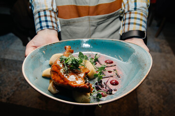 An appetizing dish on a blue plate in the hands of a girl waiter, large.