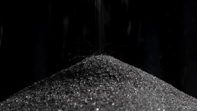 Dark sand is poured into the lower part of the hourglass with a thin trickle