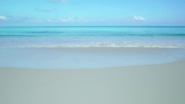 Exotic beach by the ocean with rolling waves on the sandy shore and blue sky. Timelaps