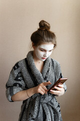 teenager u punishes face and writes a message in a mobile phone, looks into a smartphone, a clay mask on his face © Maxim