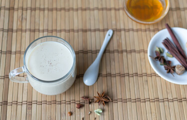 Masala tea in a glass cup with spices and honey on a wooden background. Indian beverage. Horizontal orientation. Copy space.