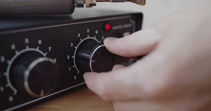 Making handmade leather belt. Young leather worker turns on electric creasing and edging machine for leather work in his workshop. Close-up of hand.