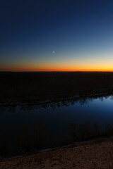 Obraz premium Young moon over the river at dusk. Bright evening sky after sunset.