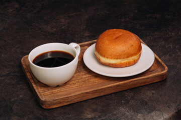 Hot coffee in white cup and fresh donut on a wooden tray. Low key. Black background. Breakfast concept