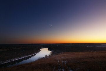 View from the hill to the moon over the river at dusk. Bright evening sky after sunset.