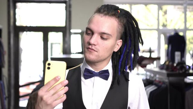 A fashionable pretentious man takes pictures of himself on a smartphone in front of a mirror in a clothing store