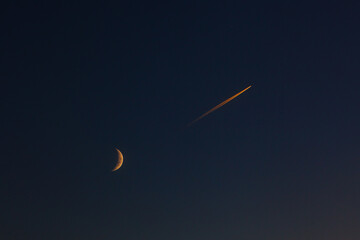 The flight of a passenger plane near the moon in the evening sky after sunset.
