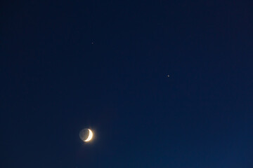 The conjunction of the Moon, Jupiter and Saturn in winter. Bright evening sky after sunset.
