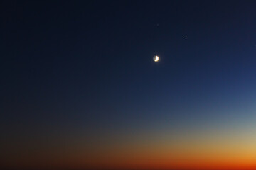 The conjunction of the Moon, Jupiter and Saturn in winter. Bright evening sky after sunset.