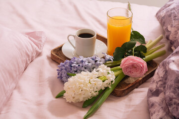 Breakfast in bed with hot coffee, orange juice and fresh flowers rose and hyacinth on a wooden tray in pink-purple bedroom. Breakfast concept