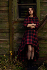 A bright girl in full growth stands against a wooden wall. A girl who looks like a witch in a red dress.