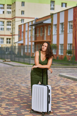 A girl adult alone stands on the street with a white traffic suitcase and holds it. Travel girl advertising vacation
