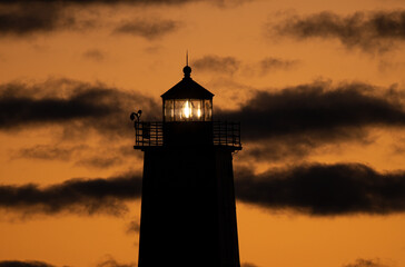 lighthouse glows in the bay under a vibrant sunset panorama