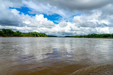 Peru, Amazonas, the large Rio Madre. Cloudy blue sky over the brown Rio Madre river. Reflection of clouds in the water.
