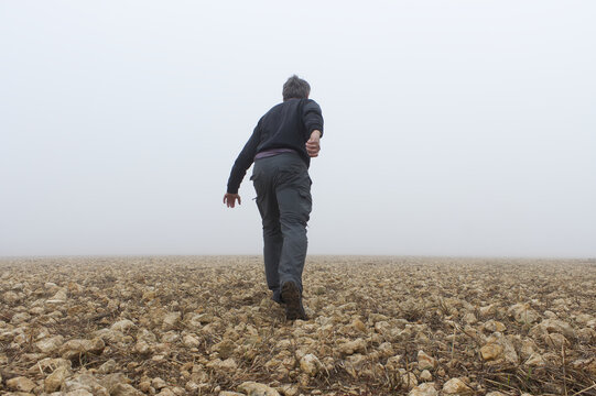 Hombre de espaldas se aleja por un pedregal hacia la niebla.


