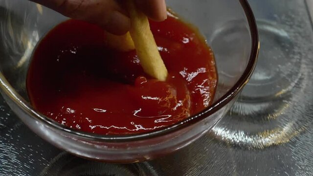 French fries dipped into ketchup in slow motion close up