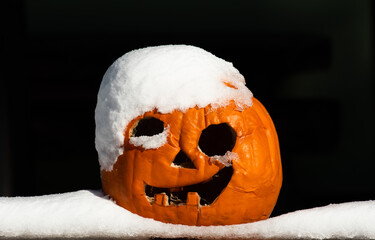 Halloween pumpkin covered with snow. Pumpkin is laying on the snow. Dark background.