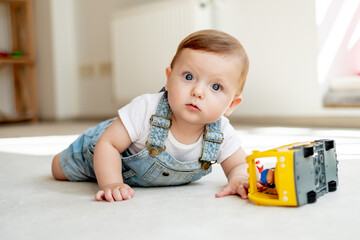 Cute baby with curious glance looking at camera, playing with toy bus in playroom