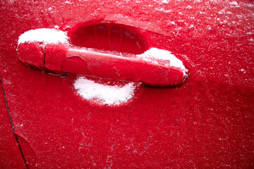 the car is frozen. the door handles are icy. frost. the car is covered with ice under the snow. red background
